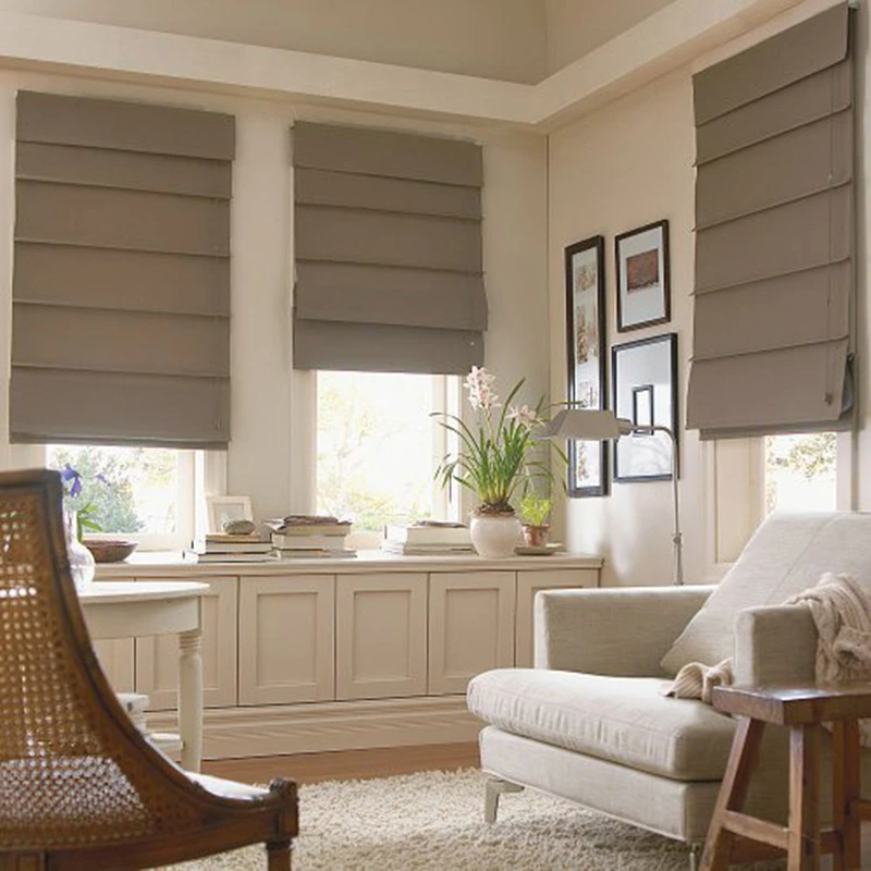 a living room with several windows covered with Roman shades. The shades are a neutral color, likely beige or light brown, which complements the room's neutral color scheme